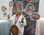 Festival participants at the NIGMS selfie station holding science themed props in front of a colorful backdrop of a cell