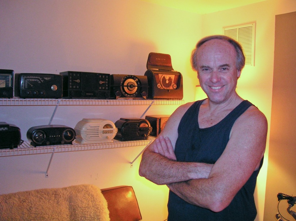 Tony, arms crossed, posing by two shelves holding rows of radios.